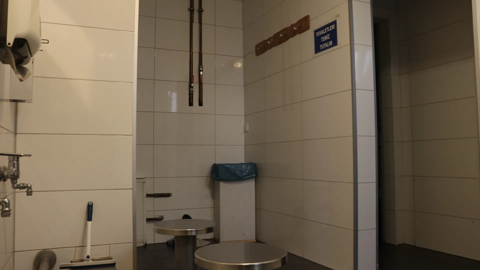 Borular, askılıklar ve „Tuvaletleri Temiz Tutalım“ levhasının bulunduğu ön hol