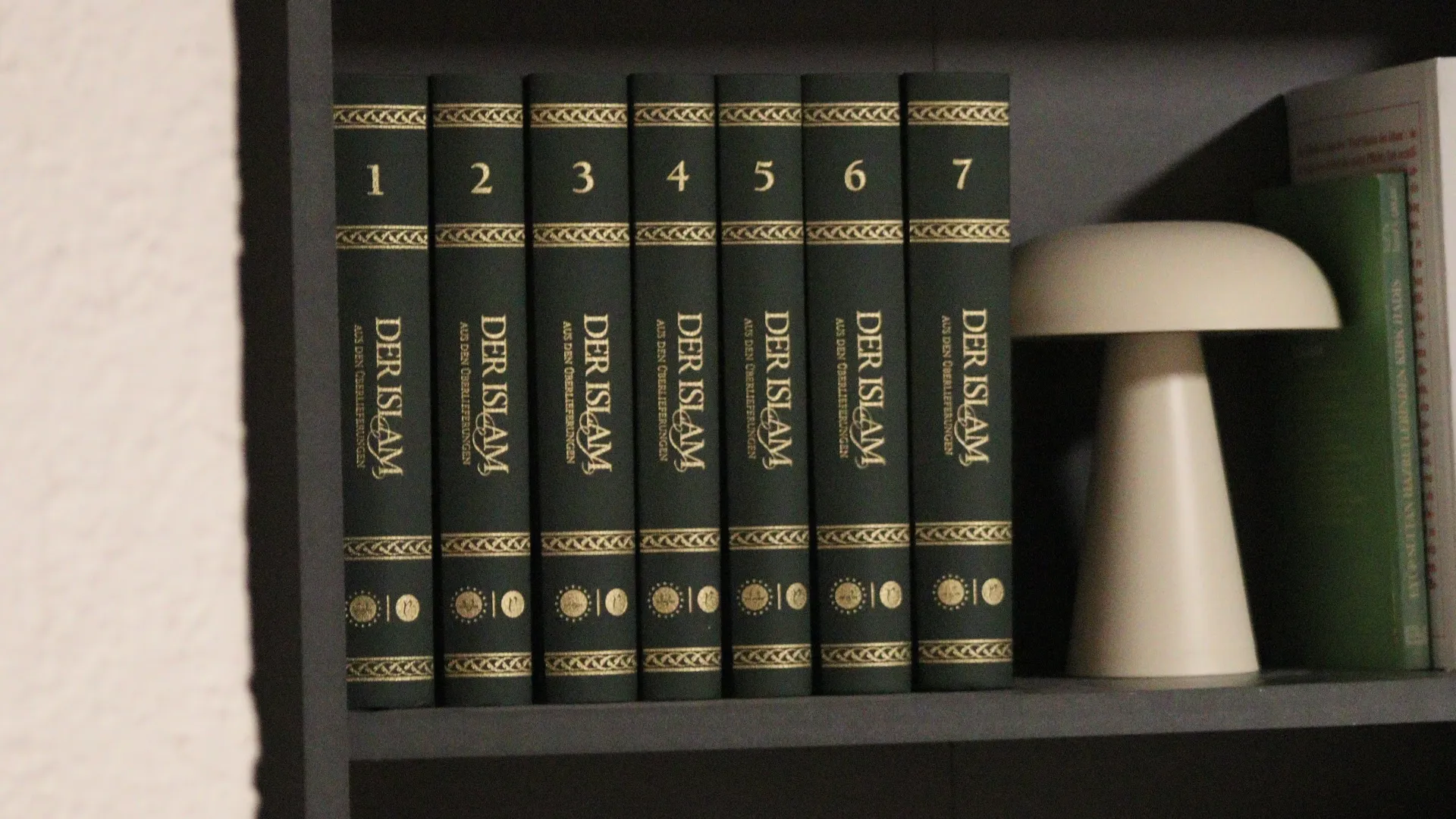 Kitaplıkta yedi ciltlik „Der Islam“ kitap serisi ve modern masa lambası