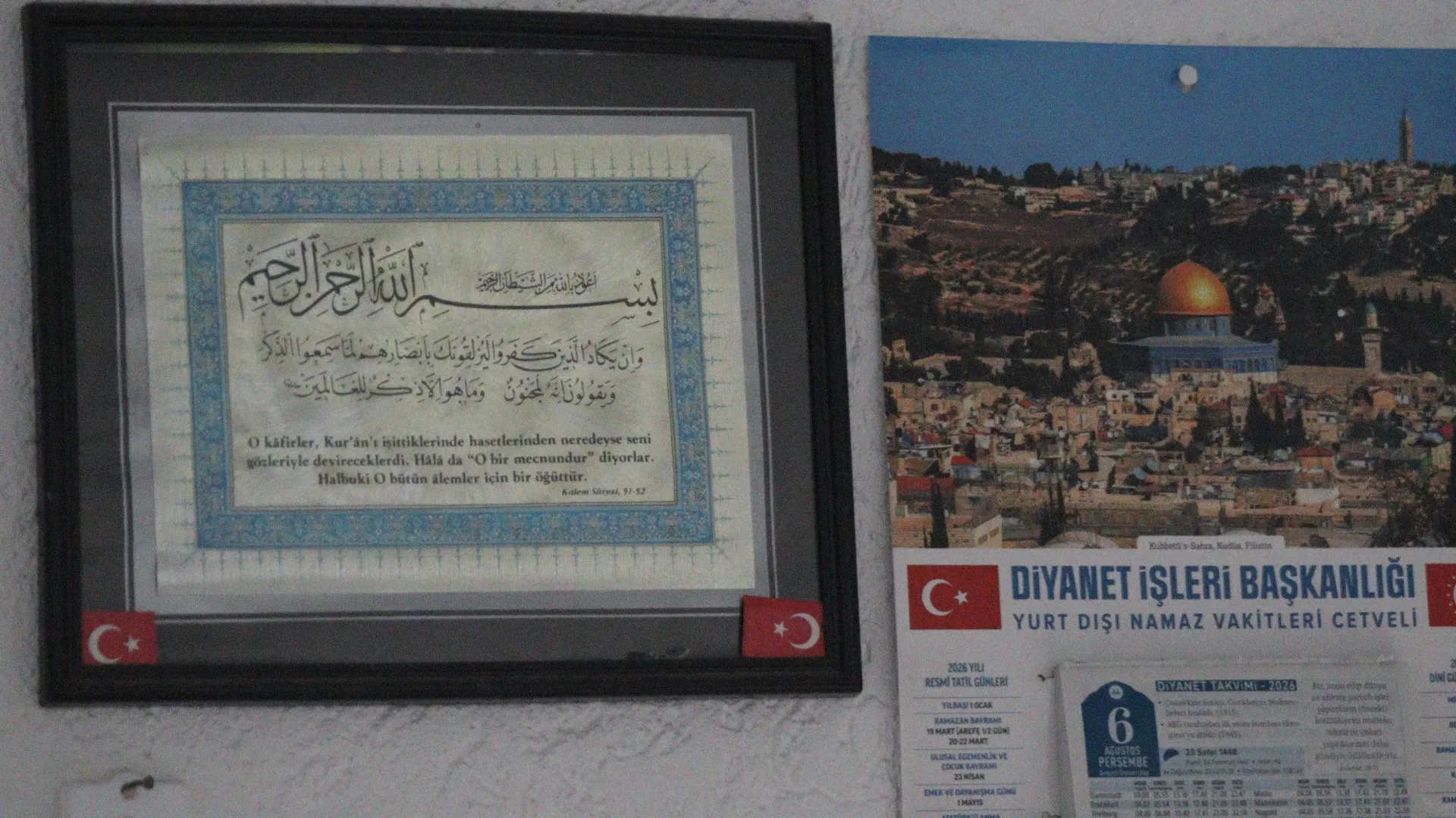 Duvar takviminin yanında Kur'an ayetleri yazılı çerçeveli hat levhası