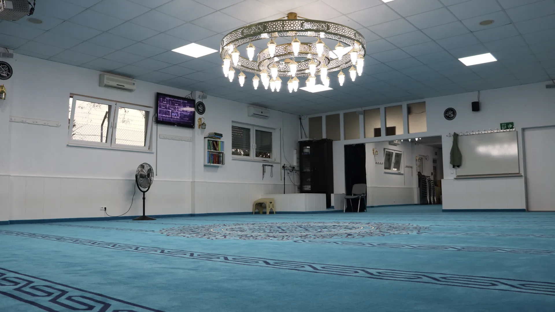 Mescitten arka duvara bakış: vantilatör, klima, duvar saati ve ekran.